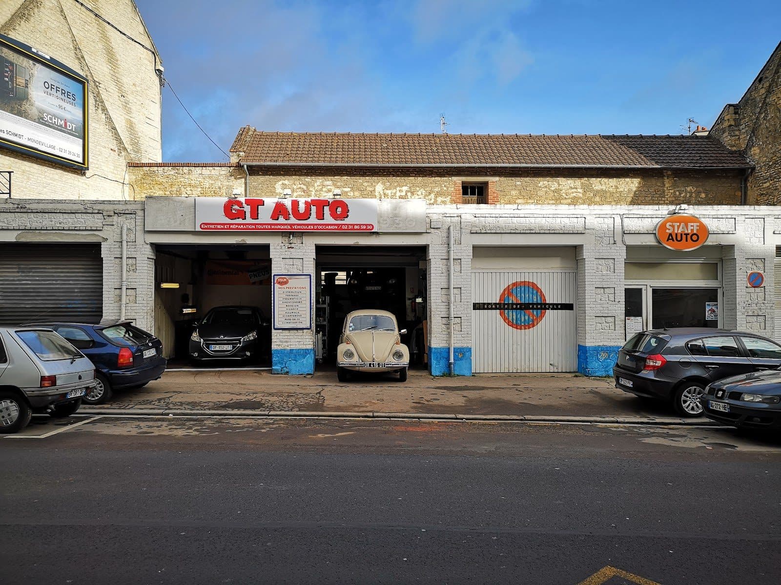 Une Volkswagen Coccinelle beige garée dans la baie de droite de GT AUTO, une Peugeot 208 noire dans celle de gauche, devanture rue de Bayeux.